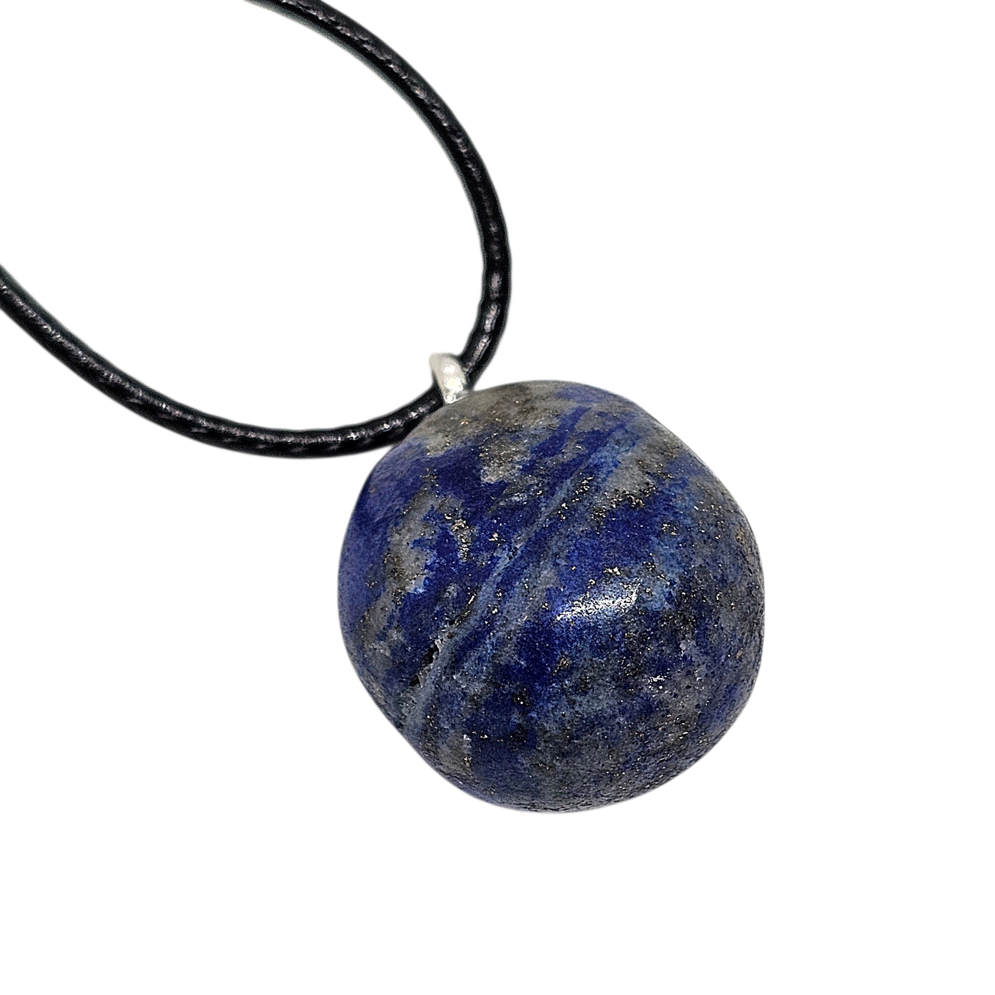 Lapislazuli Anhänger in tiefblauer Farbe mit natürlicher Struktur, an schwarzer Baumwollkordel hängend, auf hellem Hintergrund fotografiert.