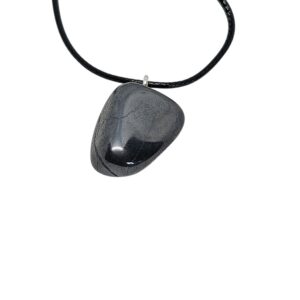 Hämatit Anhänger mit charakteristischem metallischem Glanz, an schwarzer Baumwollkordel hängend, auf hellem Hintergrund fotografiert.